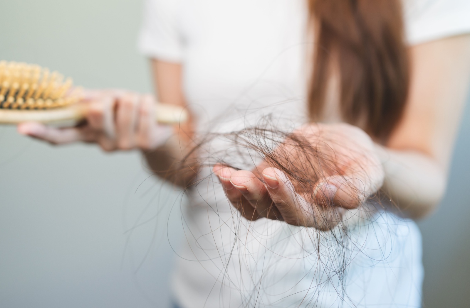 Close-up of a person holding a hairbrush in one hand a clump of hair in the other. Subject is a model.