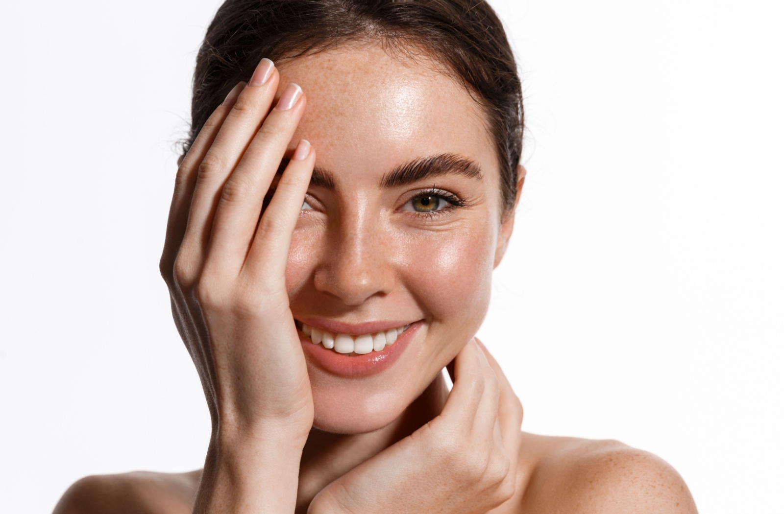 Model with clear skin smiling at the camera and half covering face with hands
